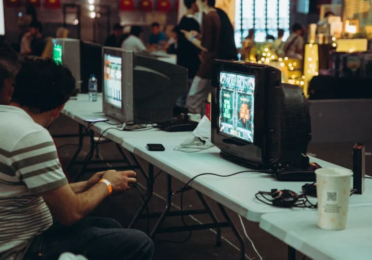 GBA Pokémon demake of Let’s Go gets English translation Adults enjoying a retro gaming event with CRT televisions and consoles, creating a nostalgic atmosphere indoors