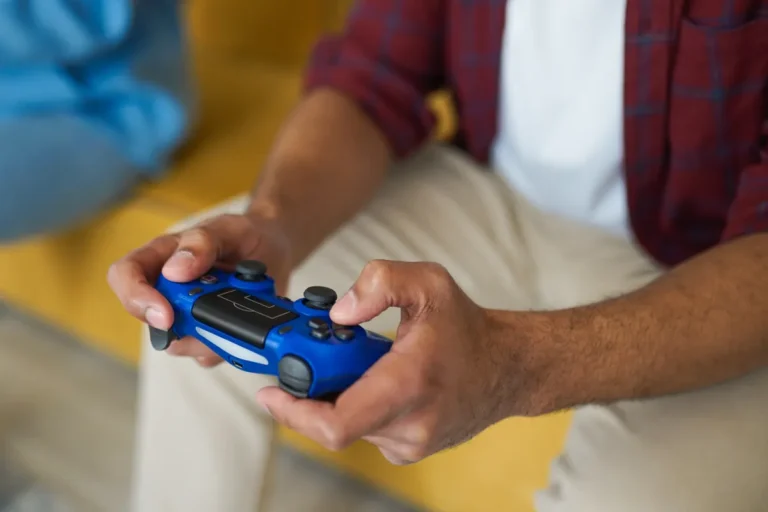 Rare Taiwanese Game Master Handheld Listed on eBay Hands holding a blue wireless game controller on a comfortable sofa indoors